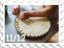 November/December 2024Potluck SWG challenge stamp - an unbaked pie on a countertop, with a baker's hands crimping the crust around the edge of the pie