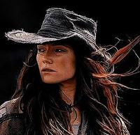 An image of Anne Bonny from Black Sails, a woman with flying red hair who looks out of the frame, wearing a wide hat. 